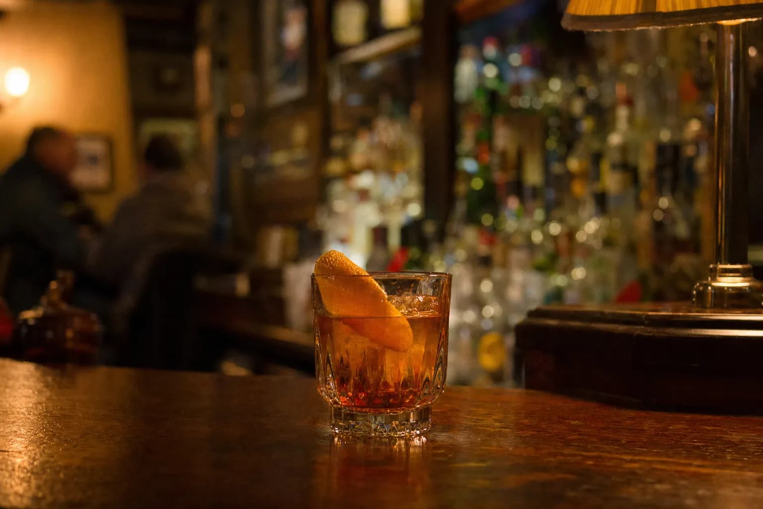 An amber cocktail with an orange twist on a dark wooden bar (AI example photo)